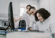 Equipe de pesquisadores trabalha em conjunto diante de um computador em um laboratório moderno.