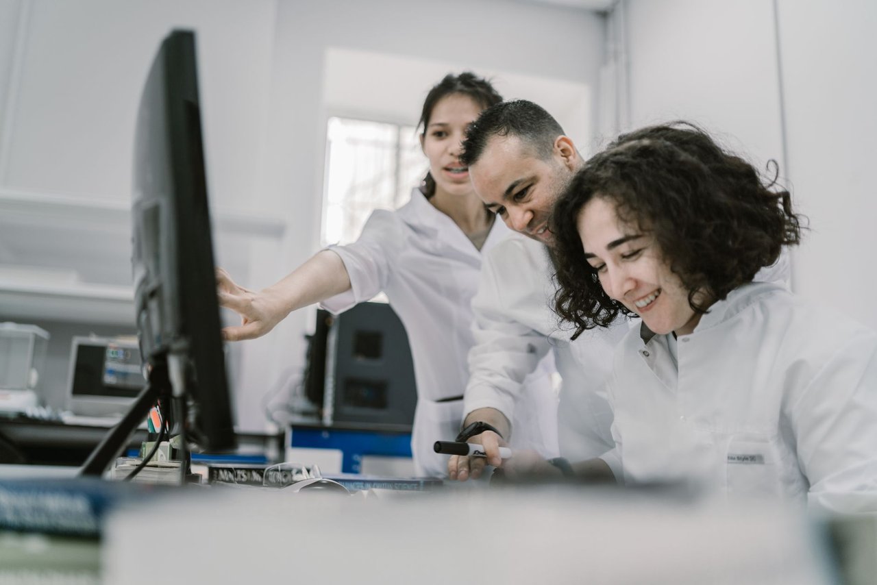 Equipe de pesquisadores trabalha em conjunto diante de um computador em um laboratório moderno.