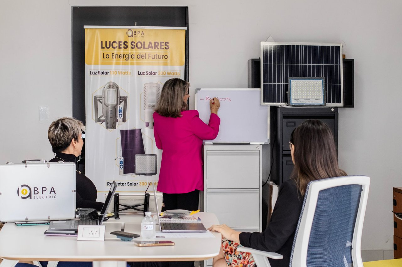 Equipe discutindo soluções de energia solar diante de painéis e quadro branco em um escritório.