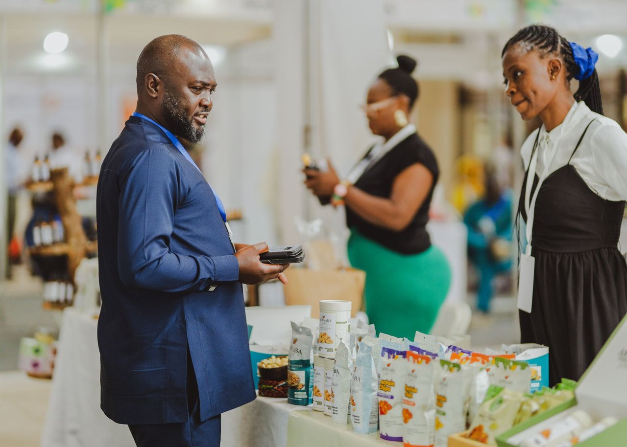 Profissionais conversam em um estande durante uma feira de negócios, com produtos expostos ao público.