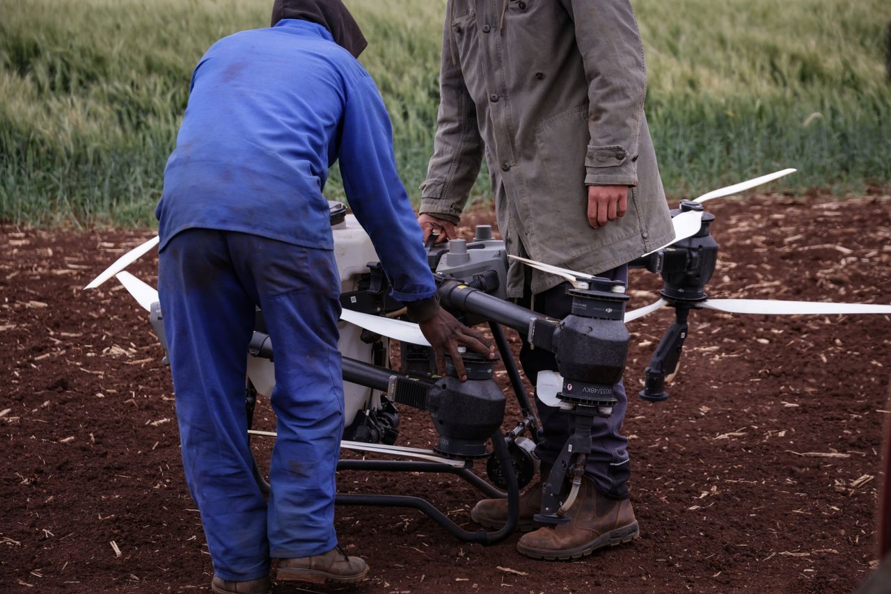 Dois agricultores operam um drone para monitorar uma plantação, destacando o uso de tecnologia no campo.