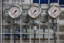 Medidores de pressão industriais instalados em uma grade metálica no interior de uma fábrica