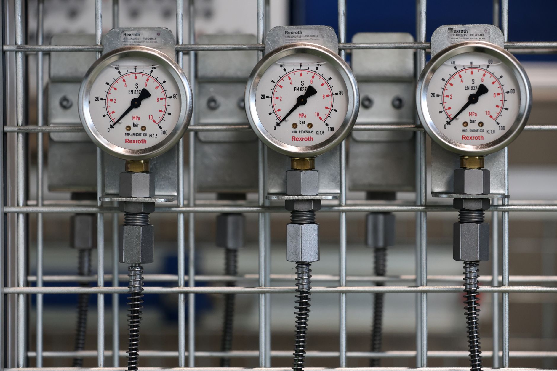 Medidores de pressão industriais instalados em uma grade metálica no interior de uma fábrica