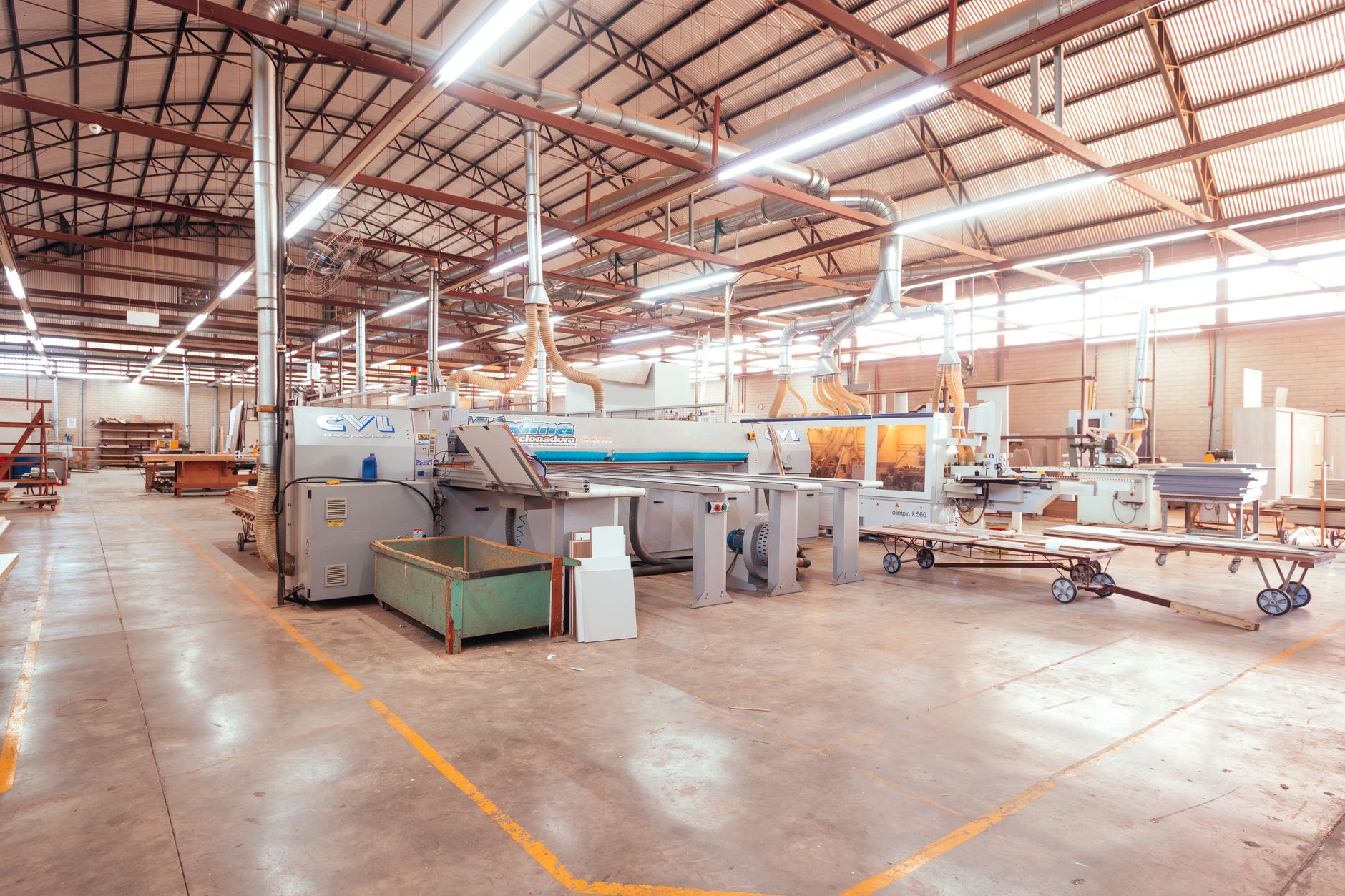Vista ampla do interior de uma fábrica brasileira organizada, com máquinas e estruturas industriais.