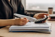 Pessoa usando uma calculadora ao lado de documentos financeiros sobre uma mesa de escritório.