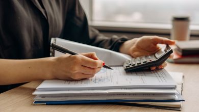 Pessoa usando uma calculadora ao lado de documentos financeiros sobre uma mesa de escritório.