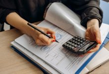 Profissional usa uma calculadora e assina documentos financeiros em uma mesa de trabalho.