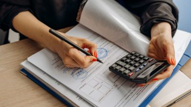 Profissional usa uma calculadora e assina documentos financeiros em uma mesa de trabalho.