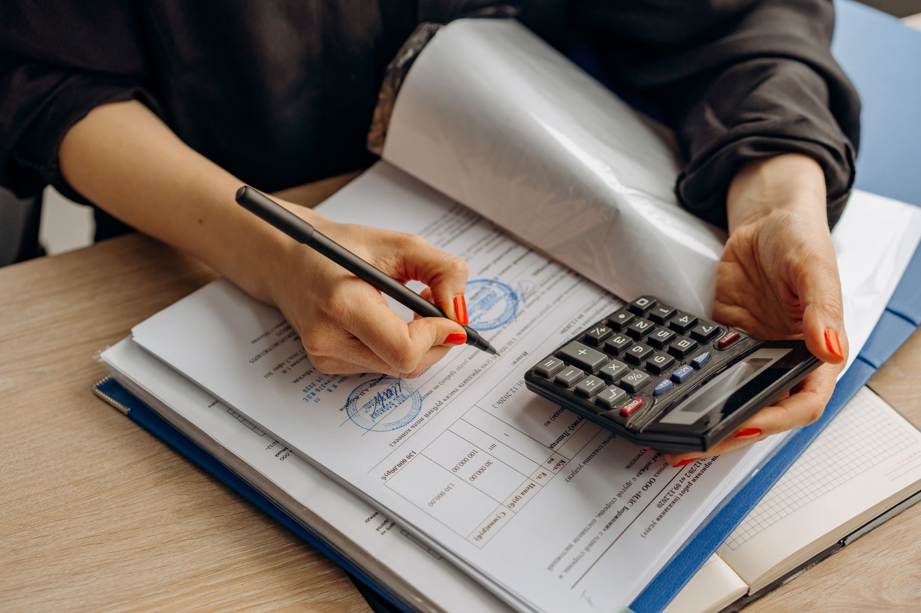 Profissional usa uma calculadora e assina documentos financeiros em uma mesa de trabalho.